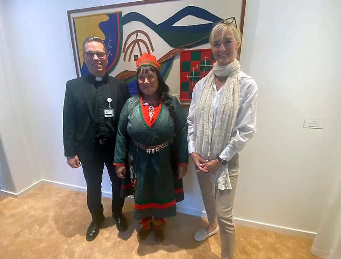 Tre personer står framför ett samiskt konstverk