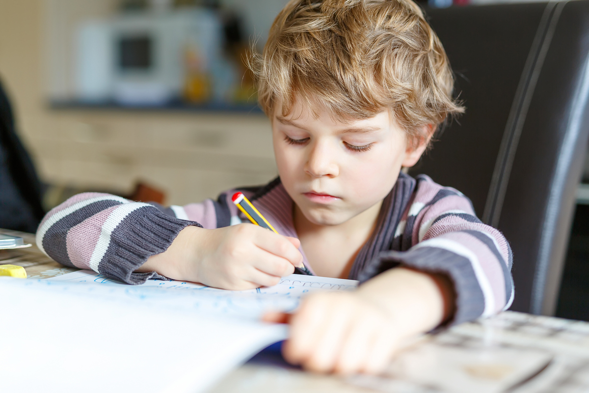 Porträtt på ett skolbarn som sitter vid skolbänken med en penna i handen och block framför sig.