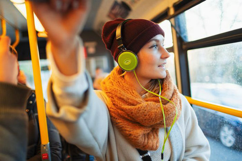 En person klädd i varm jacka, mössa, halsduk och hörlurar åker buss.