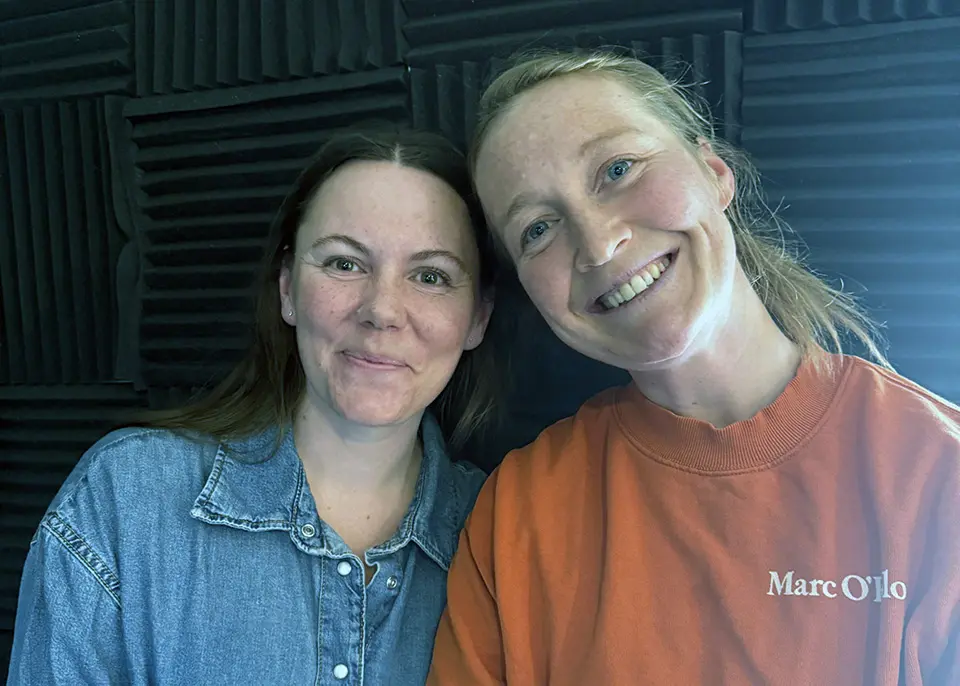 Två leende kvinnor som tittar in i bilden.