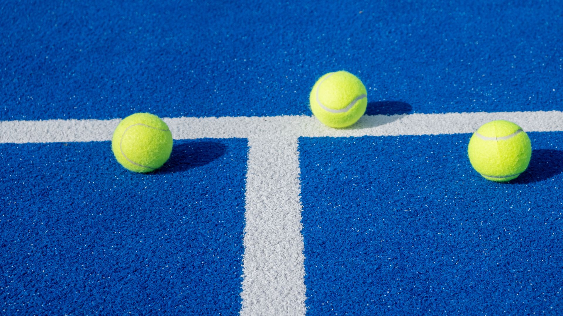 Blå heltäckningsmatta med linjer samt två padelbollar.