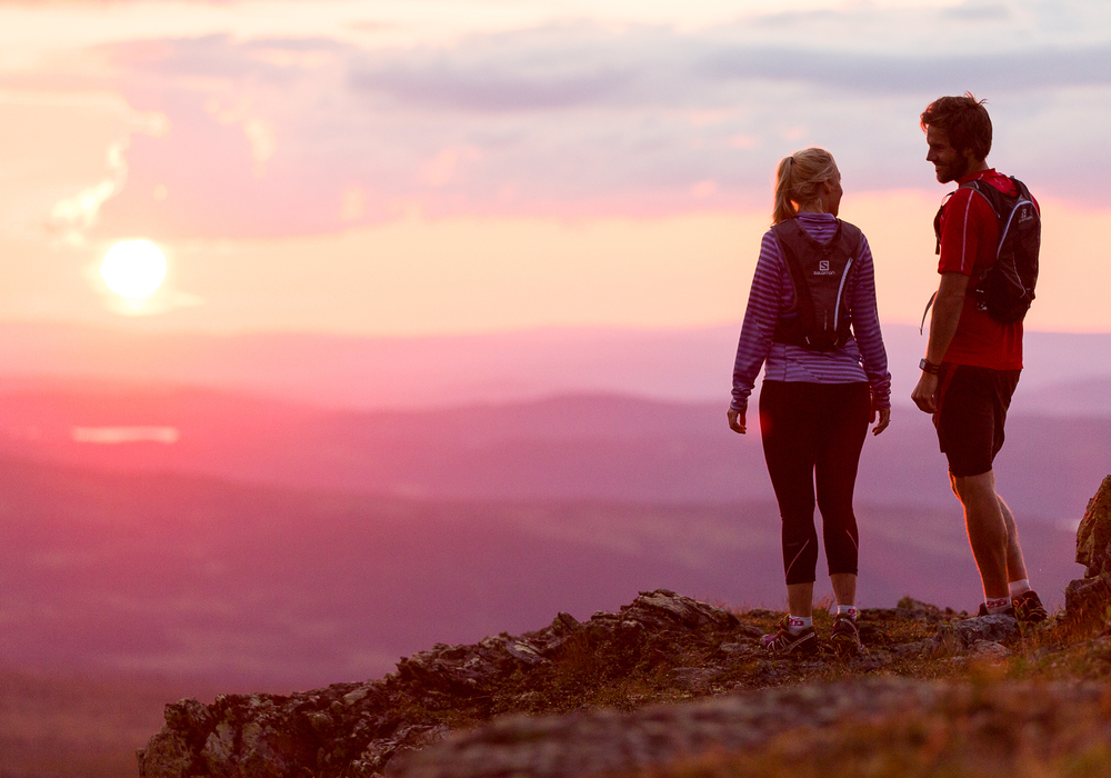 Två personer som står på toppen av ett berg i solnedgången