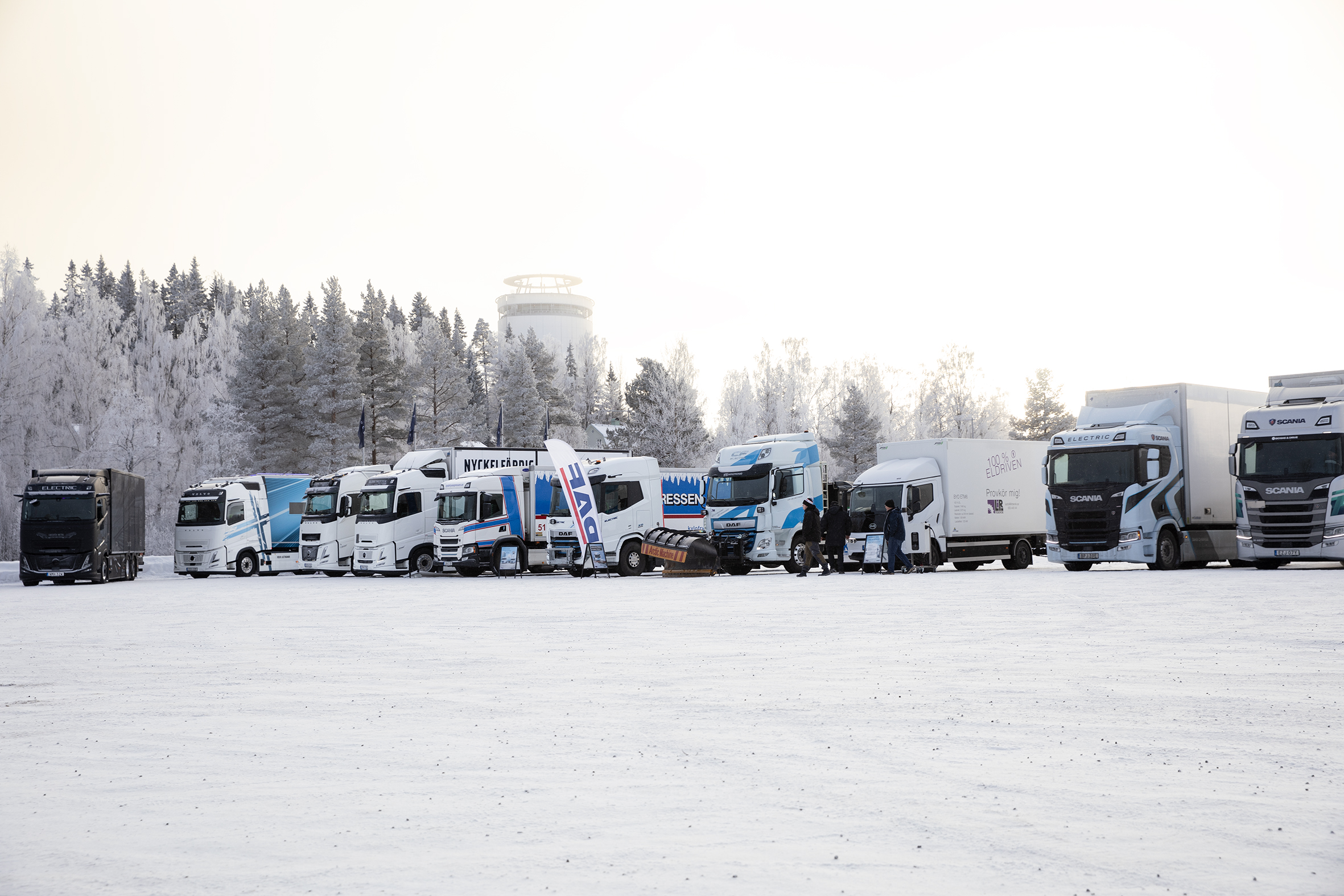 Tecknade lastbilar kör bland färgglada vägar, träd och byggnader.