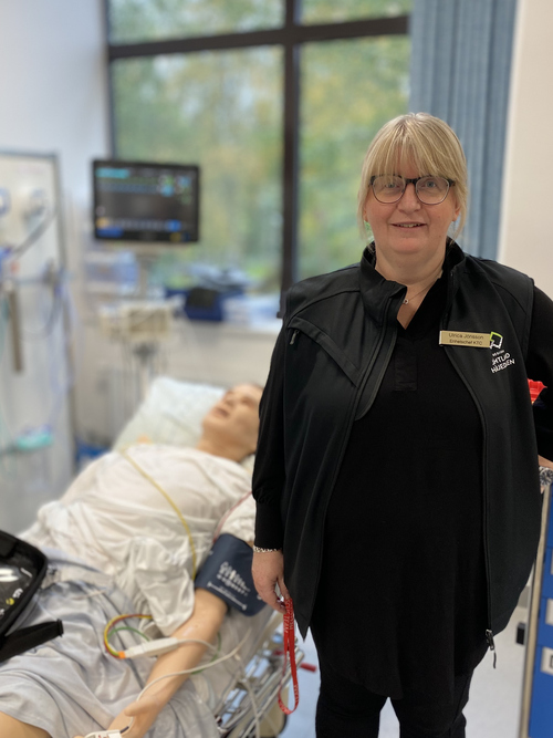 Enhetschefen på Kliniskt träningscentrum poserar framför en övningsdocka som ligger i en sjukhussäng.