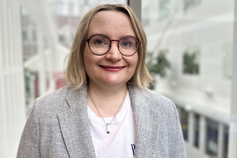 Leende person i blont axellångt hår och glasögon samt grå kavaj