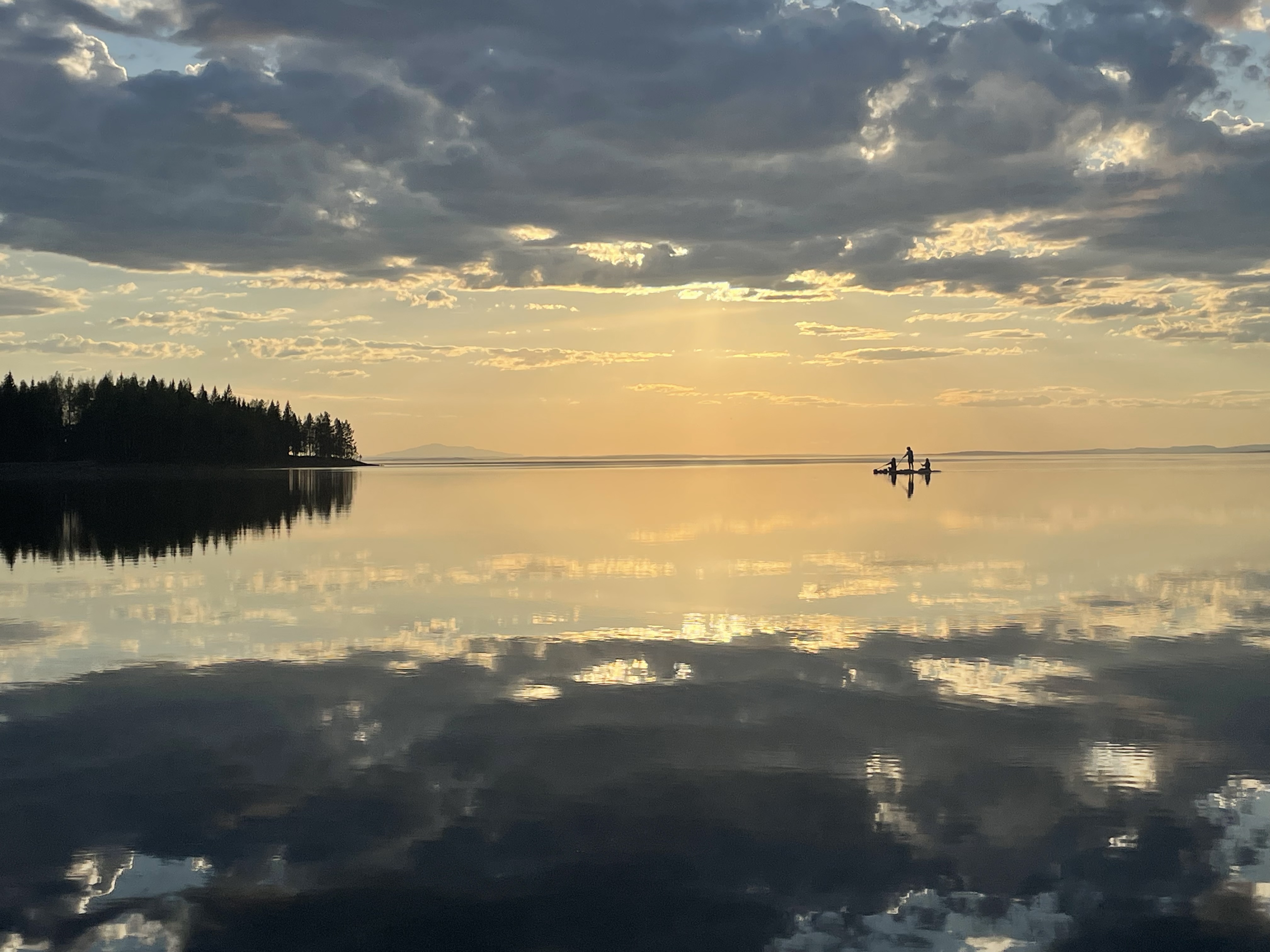 Person som på långt håll paddlar SUP i solnedgången. Spegelblank i vattnet.