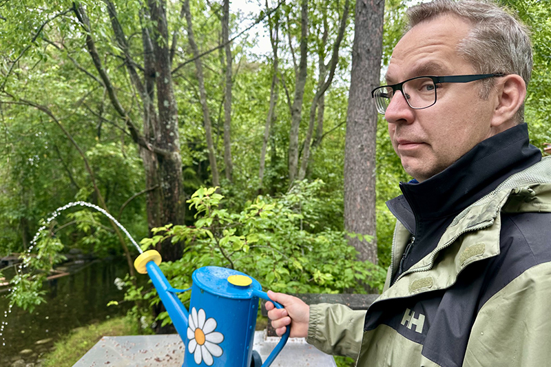 Närbild på person med glasögon som vattnar med en blommig kanna