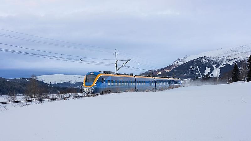 Ett tåg åker på en järnväg förbi Åre, igenom ett vintrigt fjällandskap.