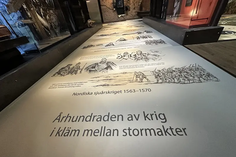 En vit matta med svart text om krigen i länet förr i tiden.