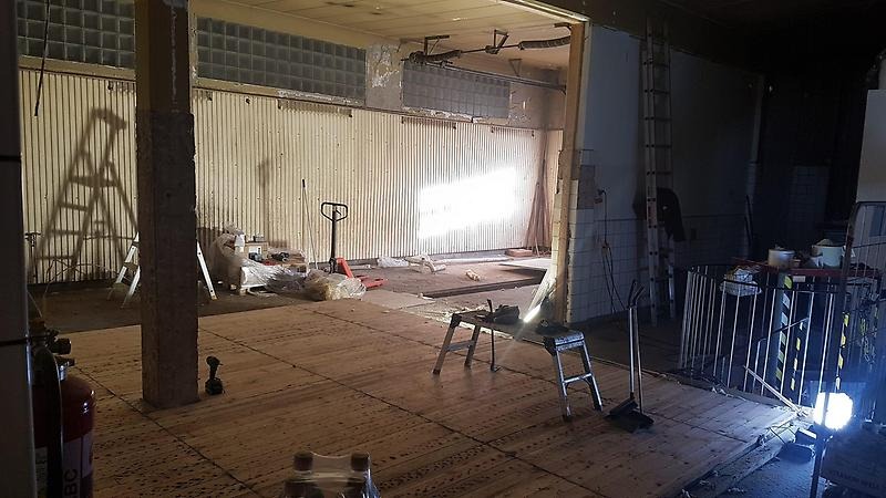 Tvätthall under renovering, med upprivna golv, plåtväggar och bygglampa.