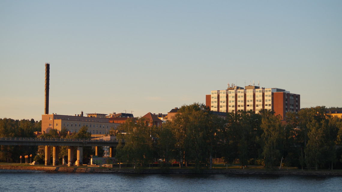 Bild på Östersunds sjukhus. Det syns träd och vatten framför byggnaden. Det är sommar ute och solnedgång.