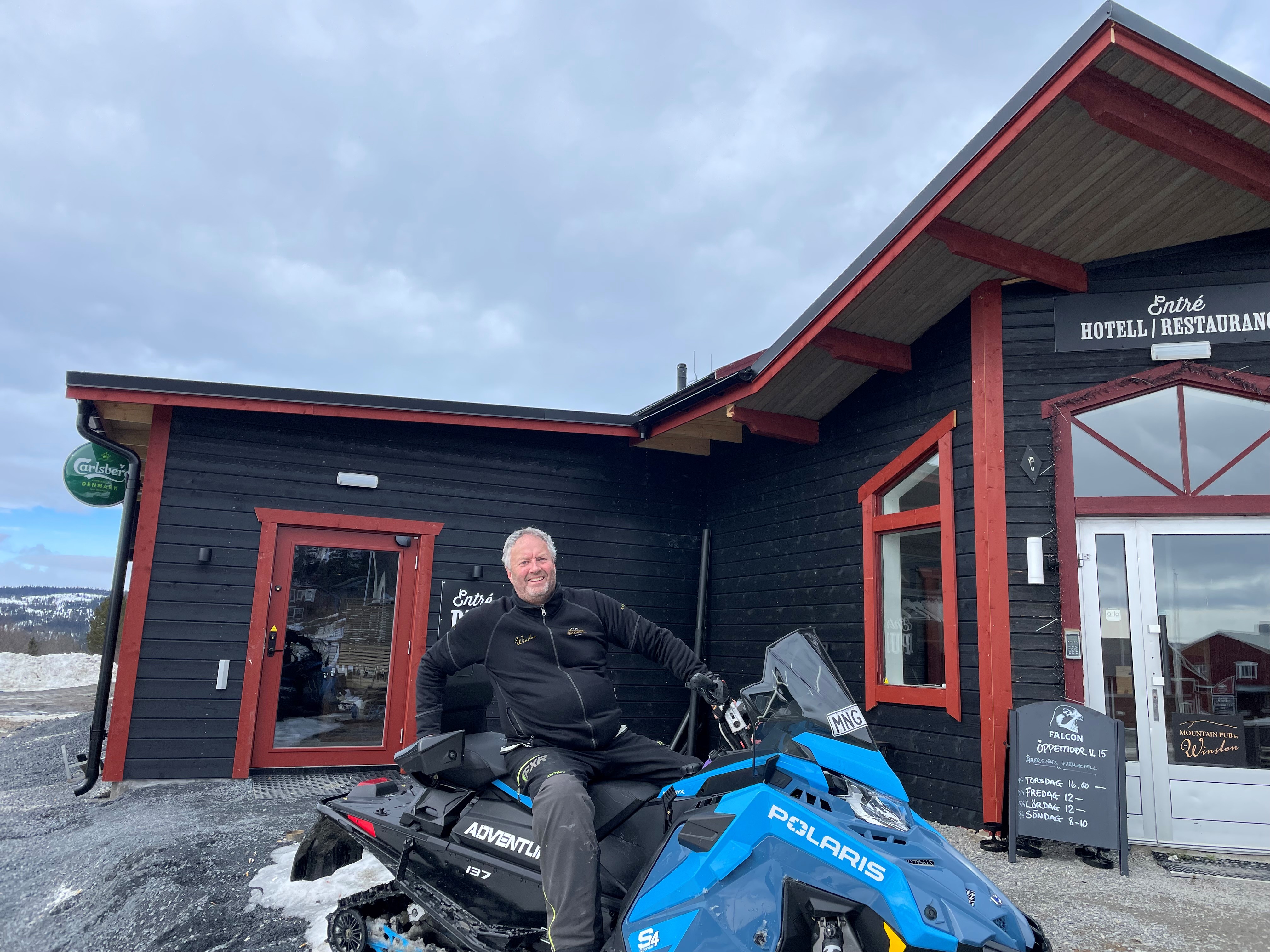 Företagaren Per-Åke Wahlund sittandes på en snöskoter utanför träfasaden till Åkersjöns fjällhotell och ingången till dess restaurang.