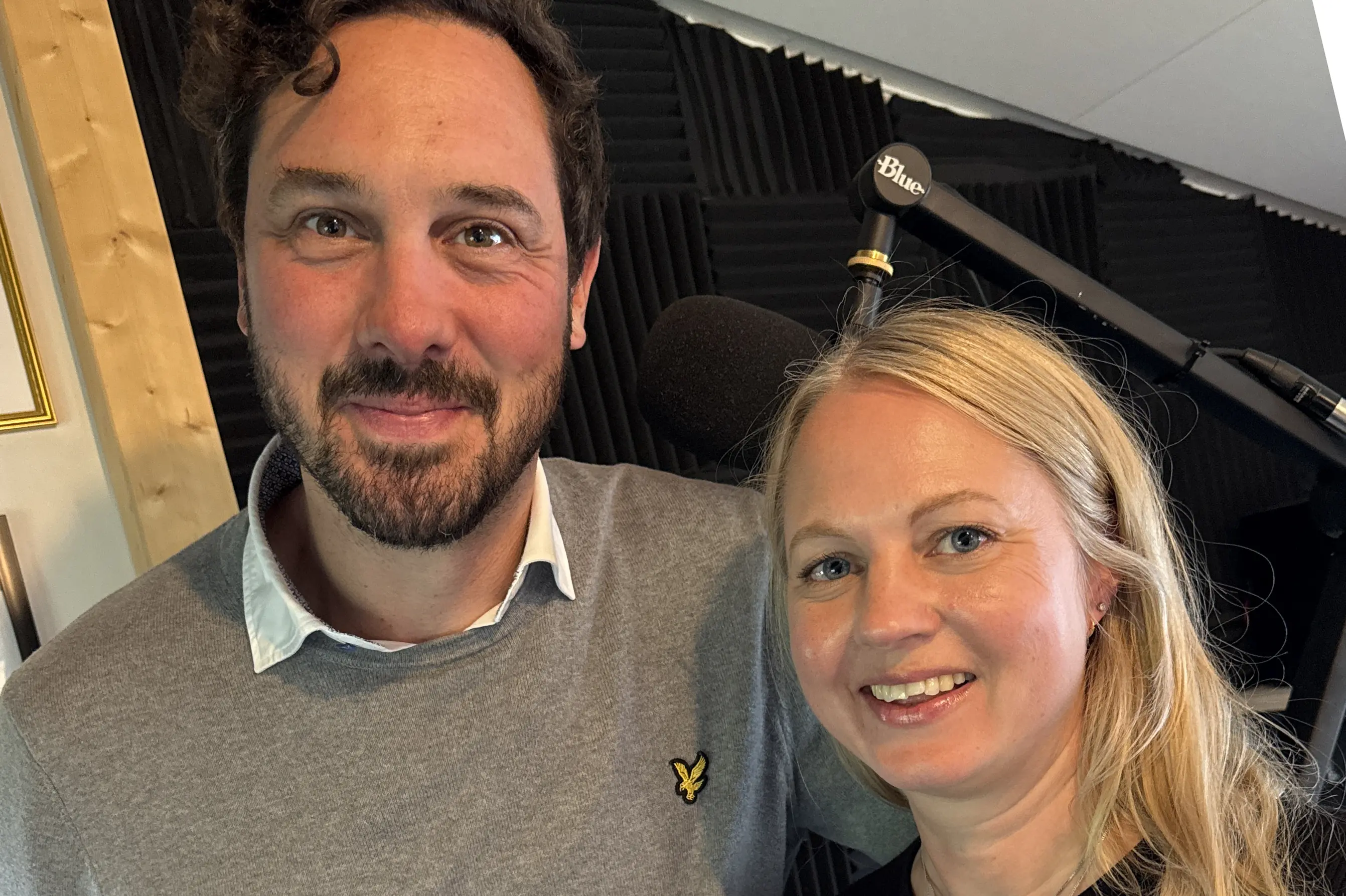 Två leende personer, en med kort mörkt hår och stickad grå tröja och en långhårig blond svart tröja.