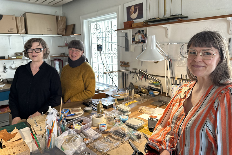 Tre personer står i en hantverksverkstad och ler mot kameran