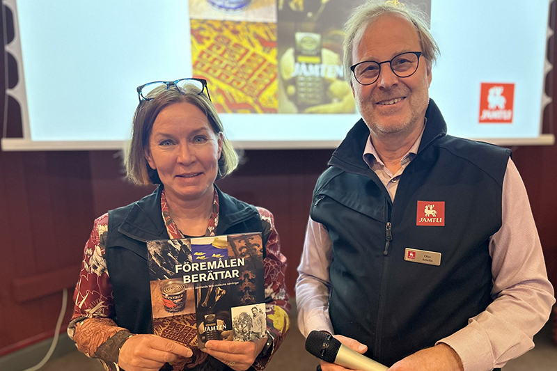 Två personer i halvkroppsformat står intill varandra och ler mot kameran. I händerna håller de upp en bok.