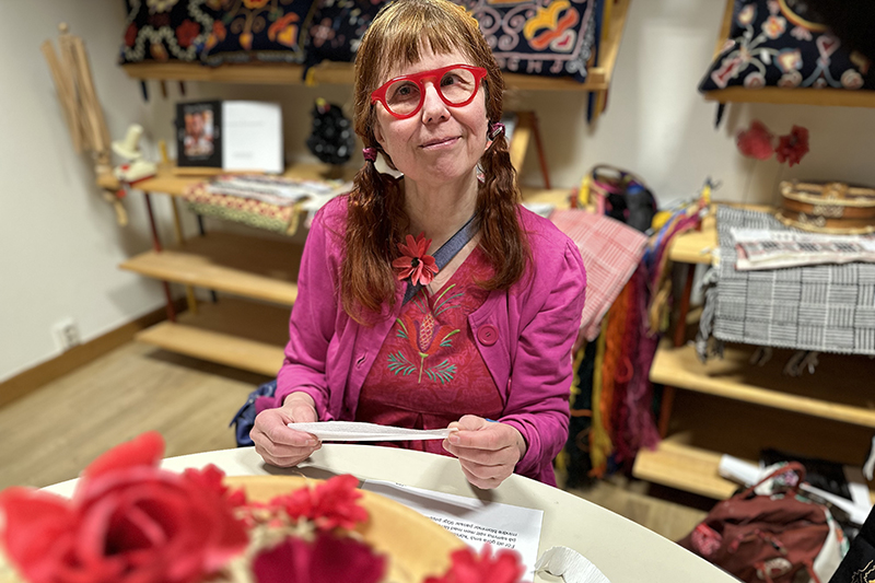 Person i rosa kläder och dito glasögon sitter vid ett träbord och skapar pappersblommor