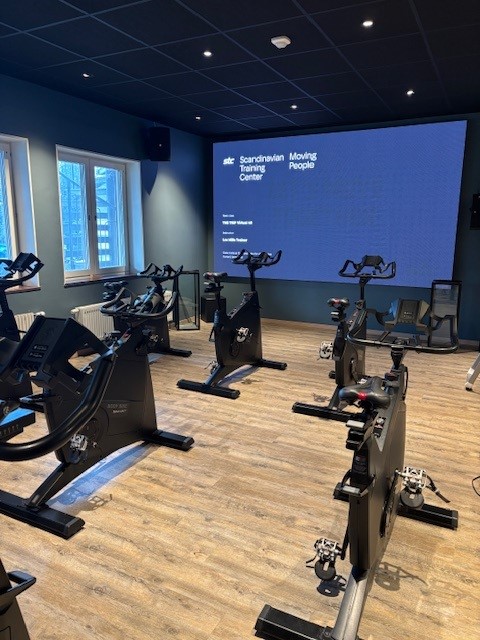En sal med spinningcyklar, en stor skärm syns längst fram i salen.