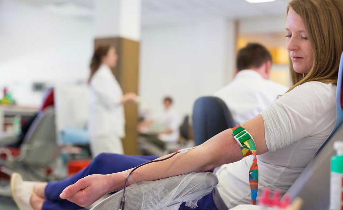 En sitter person sitter på en brits och har utrustning för blodgivning kopplad till sitt ena armveck. 