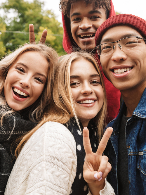 Fyra leende ungdomar som tar en selfie i utomhusmiljö.