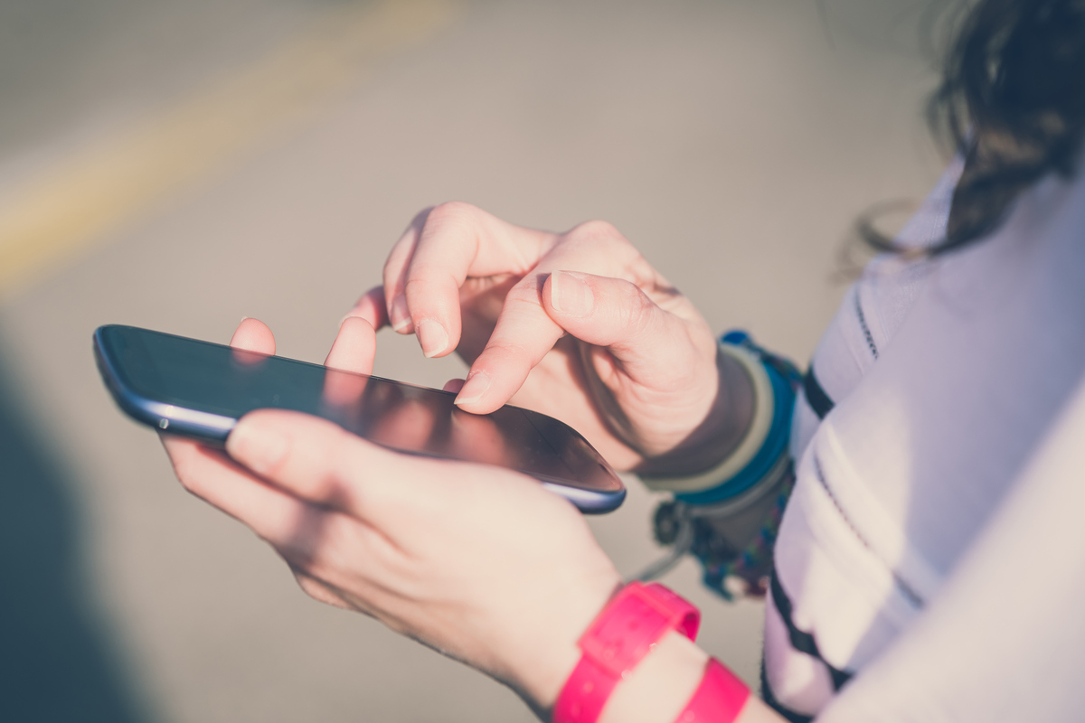 Närbild på ung persons händer som skriver på en mobiltelefon.