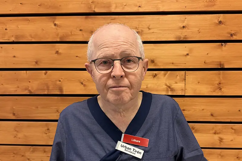 Närbild på person i vårdkläder med kort grått hår och glasögon