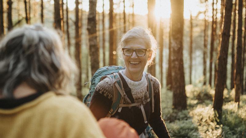 Två äldre personer ute och går med ryggsäck i skogen.