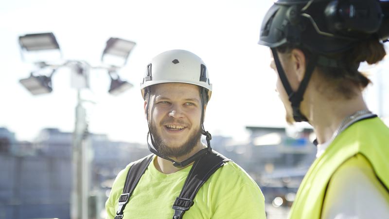 Två byggarbetare på en byggarbetslats står och pratar med varandra.