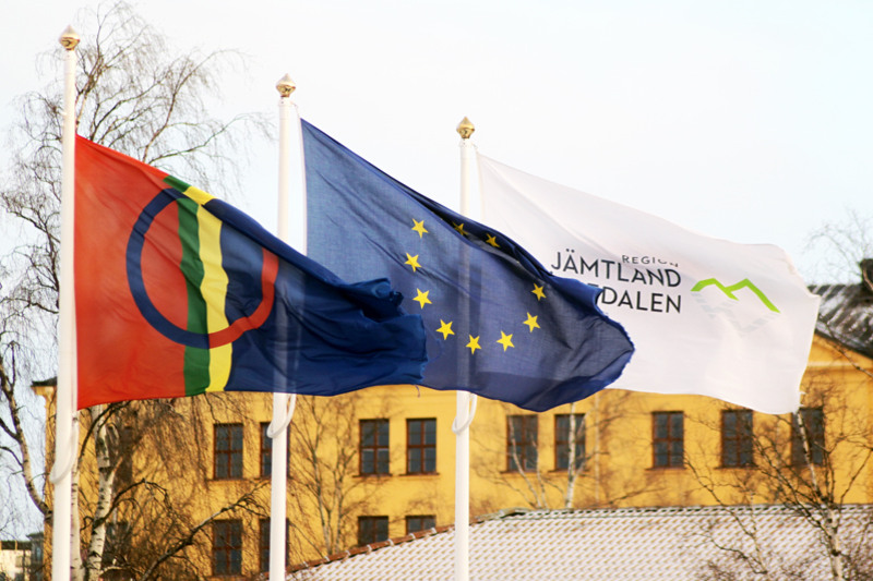 Samiska flaggan, EU-flaggan och Region Jämtland Härjedalens flagga hissade i flaggstänger bredvid varandra utanför Regionens hus i Östersund.