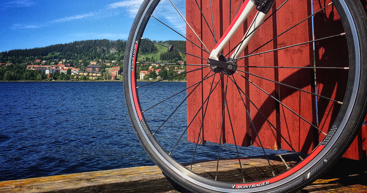 Närbild på cykelhjul med en röd vägg och blått vatten i bakgrunden