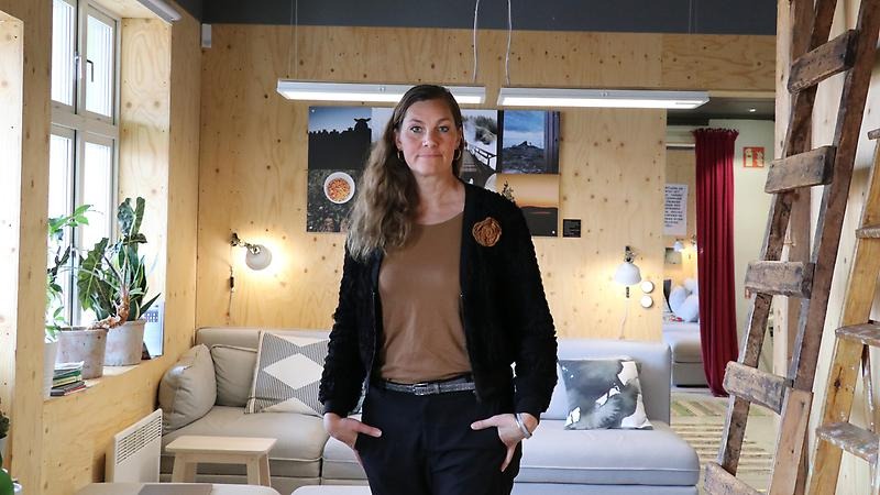 Porträttbild på företagaren Sara Carlemår som står upp med händerna i fickorna och allvarsam uppsyn, i kontorsmiljö.