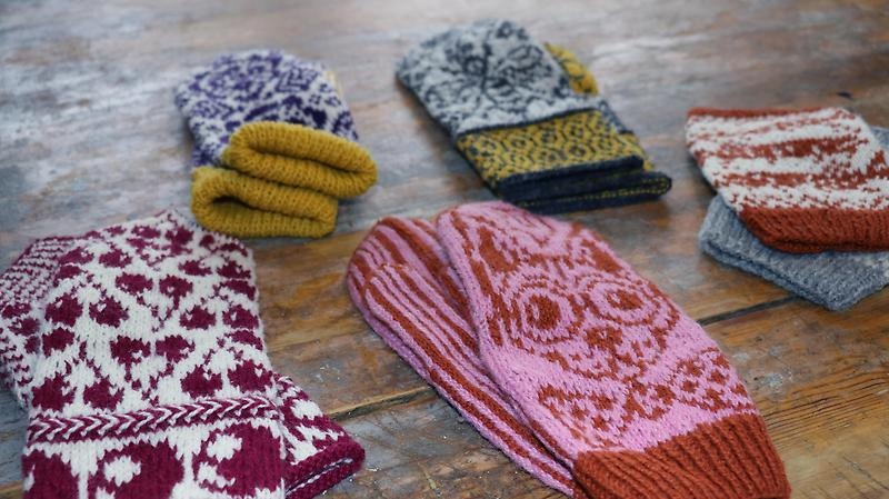 Närbild på stickade vantar i olika färger och mönster.