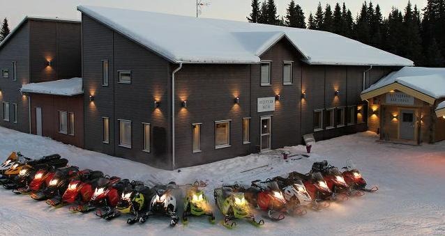 Brun hotellbyggnad med ytterbelysning och en rad snöskotrar parkerade utanför. Foto: Berne Brenje