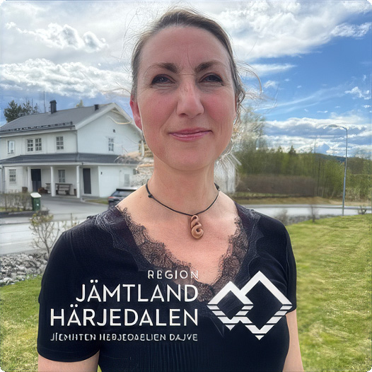 En kvinna med uppsatt hår iklädd ett svart linne med spetskrage och halsband står utomhus och tittar mot betraktaren