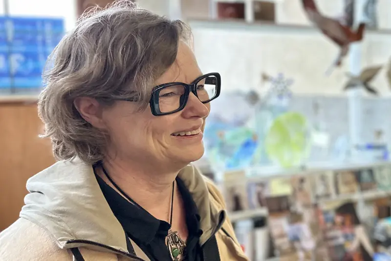 Foto på leende person i kort lockigt hår med markerade mörka glasögonbågar