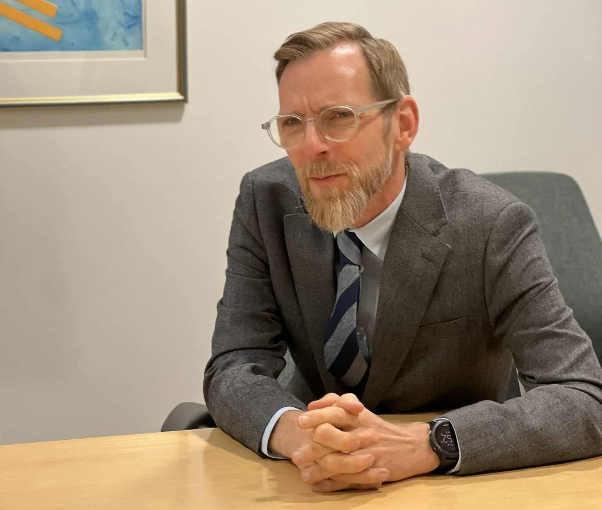 En man sitter vid ett skrivbord med knäppta händer och blicken riktad över bordet.