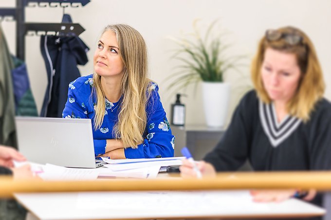 Två personer vid ett konferensbord, en kvinna i fokus som tittar upp mot vänster mot en planeringstavla