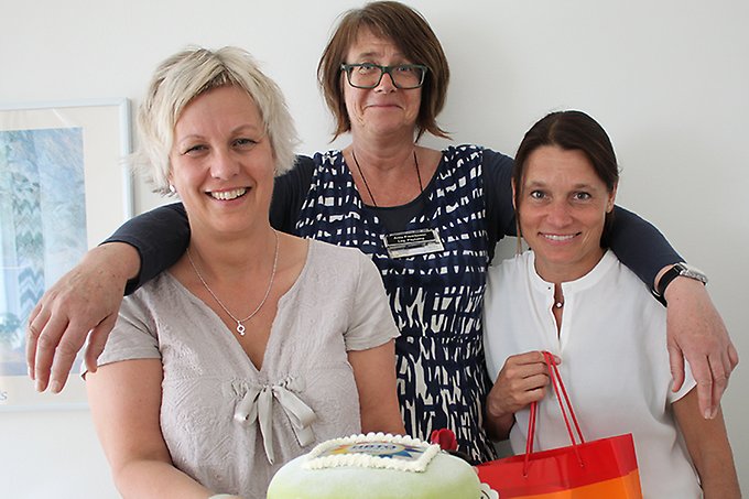 Tre kvinnor står tätt ihop och håller i en tårta i sina armar