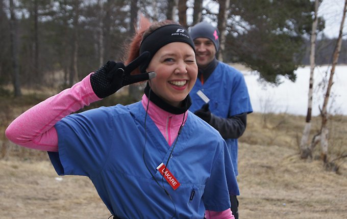 En kvinna iklädd löparkläder gör v-tecknet och ler mot kameran. I bakgrunden står en man i löparkläder.