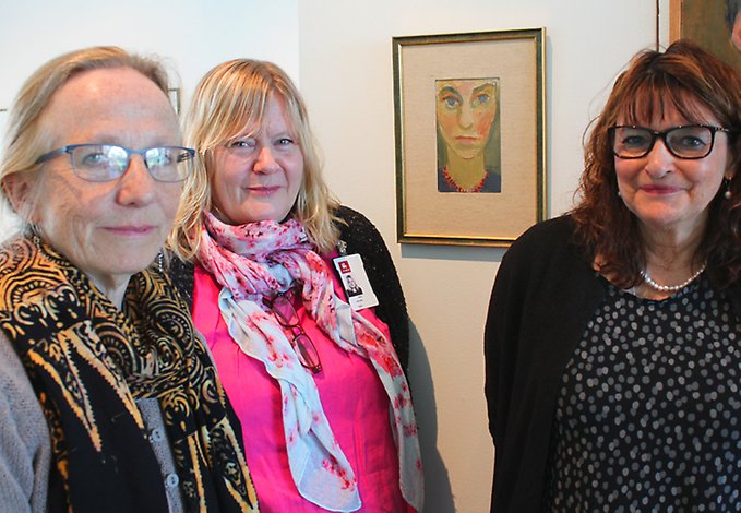 Tre kvinnor står tätt ihop framför ett självporträtt av en fjärde kvinna