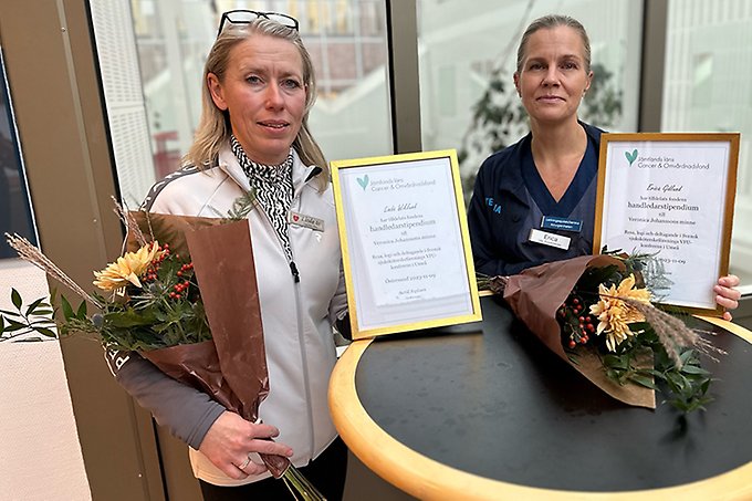 Två personer står vid ett runt bord med diplom och varsin blomsterbukett