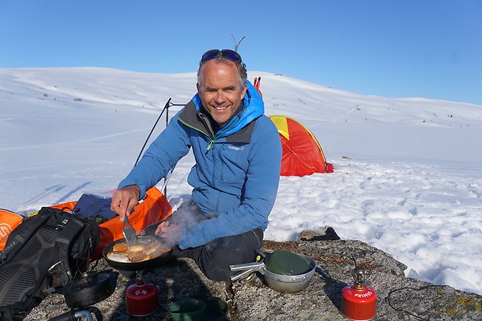 Porträttbild på Tore Holand, styrelseordförande för Blåsjöns framtid Ek. F. Han sitter ute i ett vinterlandskap vid ett tält och steker mat på stormkök. 