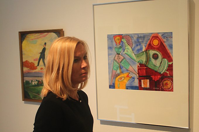 En kvinna, Christina G. Wistman, står bredvid ett konstverk och tittar halvt mot kameran