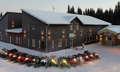 En brun hotellbyggnad i vintermiljö, med mysig utebelysning och en hel rad skotrar parkerade utanför.