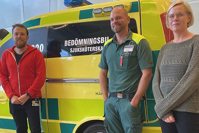 Tre personer står utanför en ambulans och tittar in i kameran