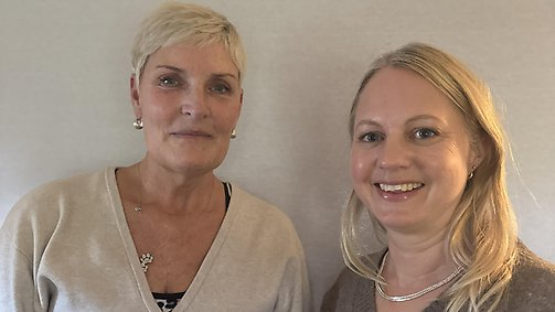 Två personer står bredvid varandra framför en vit vägg.