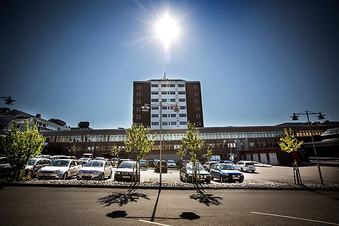 Östersunds sjukhus fotograferat från utsidan, bilar står parkerade framför byggnaden och solen skiner från blå himmel.