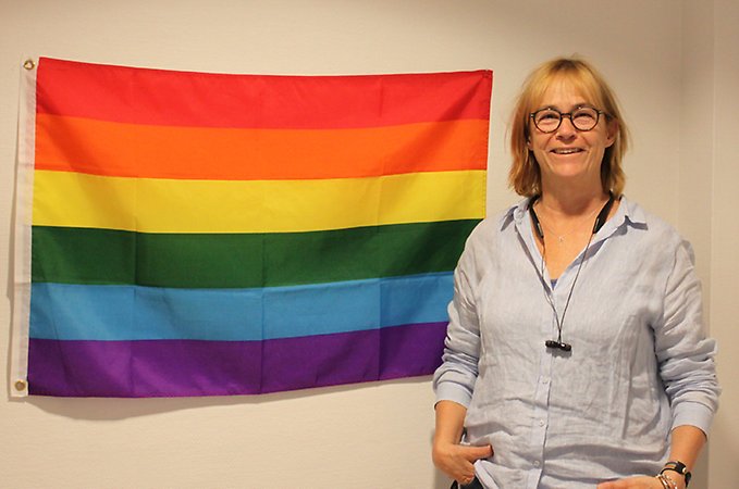En leende kvinna står framför en regnbågsfärgad flagga