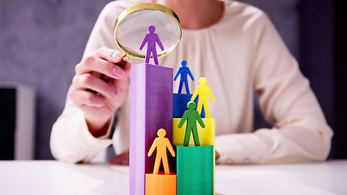 En person sitter med förstoringsglas över ett par färgade staplar med figurer på.