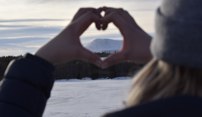 Närbild på en person som formar ett hjärta med sina båda händer. Genom hjärtat syns Sonfjället i bakgrunden.