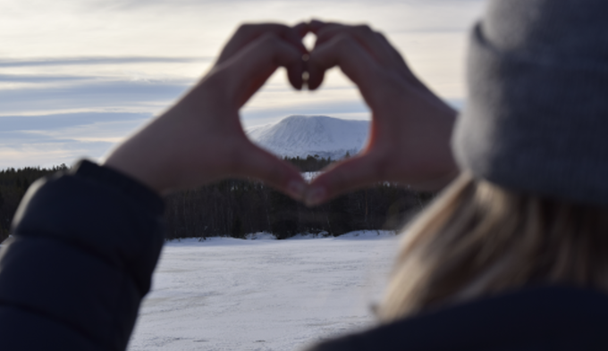 Närbild på en person som formar ett hjärta med sina båda händer. Genom hjärtat syns Sonfjället i bakgrunden. 